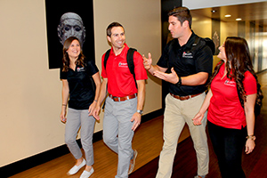 Students walking in SDSU attire down a hall